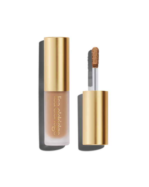 A closed bottle of Lisa Eldridge Liquid Silk Liquid Eyeshadow in mauve beige shade Phoebe, with a gold cap containing an applicator wand with product on it, against a white background.